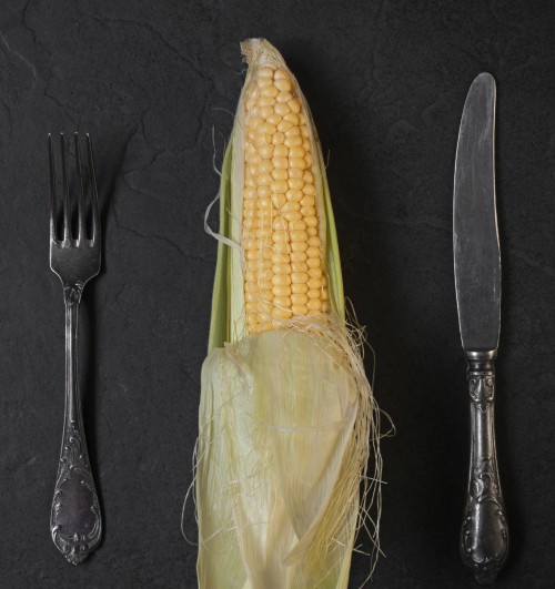 Corn, fork and knife on the black table