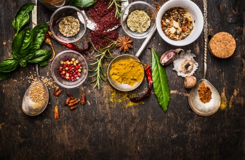 Dry colorful spices in spoons and bowls with fresh seasoning on dark rustic wooden background, top view, border