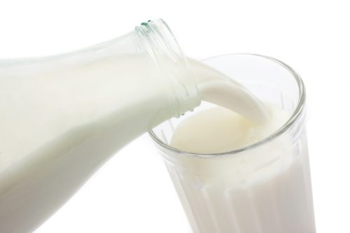 Fresh milk pouring from the glass bottle to the glass